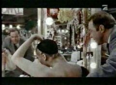 Showgirls movie. Topless girl is putting on bob black wig on her tight black wigcap.